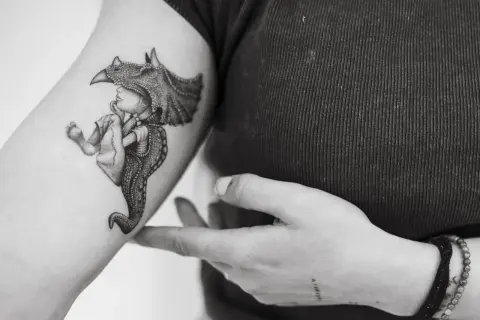 Un tatuaje de un niño con un casco de dinosaurio, con detalles intrincados, que evoca la magia de los tatuajes sevillanos.