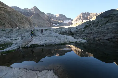 Randonneurs traversant un paysage rocheux près du lac du Portillon, avec des montagnes imposantes en arrière-plan.
