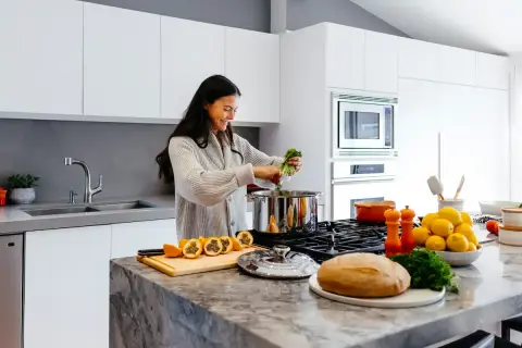 Kvinna lagar mat i ett modernt kök. Frukt, bröd och grönsaker ligger på bänken, bra spartips mat.