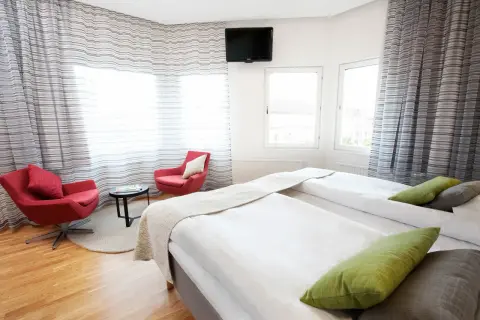 Ett modernt hotellrum med två sängar, röda fåtöljer och utsikt över en plaza i Borås.