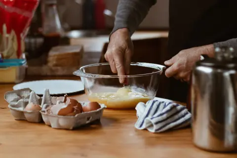 Préparation d'une crème pâtissière façon Cyril Lignac : des œufs battus dans un bol, des coquilles d'œufs à côté.