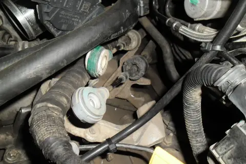 Widok na mechanizm skrzyni biegów z widocznymi linkami zmiany biegów, przewodami i elementami silnika.
