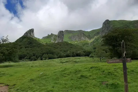 Paysage montagneux verdoyant avec des formations rocheuses spectaculaires. Un panneau indique "Fond de vallée", peut-être le chemin vers la cascade de la biche.