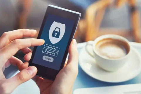 Dłoń trzyma smartfon z ekranem logowania do bankowości internetowej. Widoczne pole na hasło i ikonka kłódki symbolizują bezpieczeństwo.