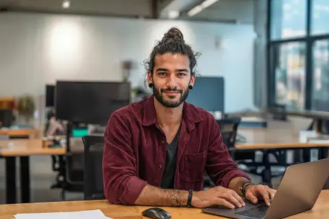 Junger Mann mit Dutt am Laptop, lächelnd. Ein zukünftiger marketing master hamburg.
