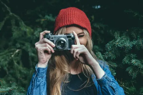 Dziewczyna w czerwonej czapce i dżinsowej kurtce trzyma aparat, gotowa do uchwycenia piękna przyrody. To jej dzień fotografa.