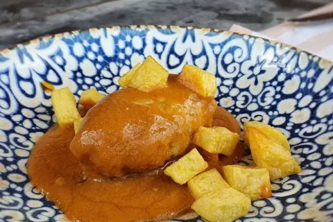 Rollo de bonito asturiano bañado en salsa, acompañado de patatas fritas en dados, servido en un plato azul y blanco.