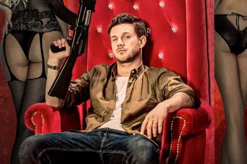 Mężczyzna z bronią na czerwonym tronie, otoczony przez kobiety w bieliźnie. Typowy plakat filmowy Patryka Vegi.