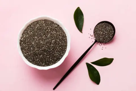 Semi di chia in una ciotola e un cucchiaio, con foglie verdi. Un aiuto naturale per la menopausa.