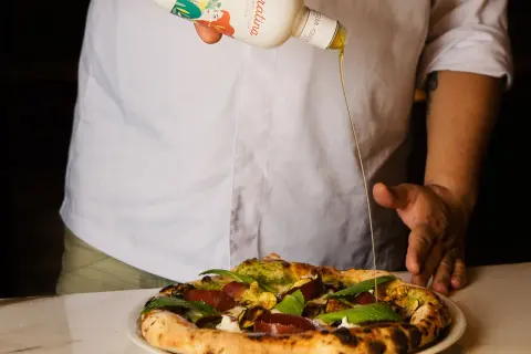 Un cuoco versa l'olio Coratina migliore su una pizza gourmet. L'olio extra vergine d'oliva esalta i sapori.