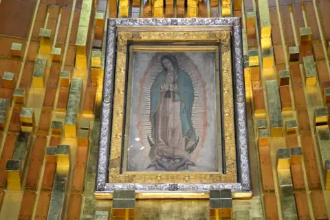 Obraz Matki Boskiej z Guadalupe, którego niezwykłe właściwości badała NASA, w złotej ramie na tle drewniano-złotej ściany.