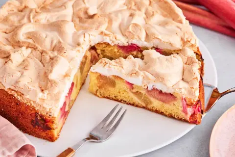 Saftiger Rhabarberkuchen mit luftigem Baiser, ein Stück ist schon angeschnitten.
