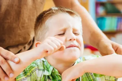 Chłopiec zamyka oczy, zaciska pięść, a dorosły trzyma go za ramię. Szukamy odpowiedzi, jak leczyć ADHD, by pomóc dzieciom.