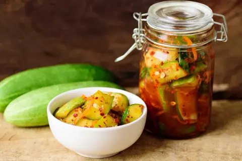 Słoik i miseczka z pikantnymi ogórkami z papryką chili, obok świeże ogórki.