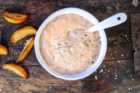 En skål med krämig hamburgerdressing, perfekt för ditt nästa hamburgerdressing recept. Serveras med klyftpotatis på en träbakgrund.