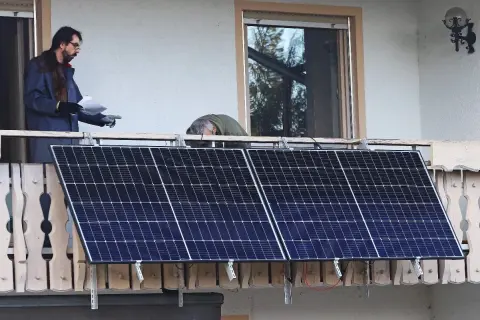 Dos hombres instalan placas solares en una terraza. Uno revisa un papel mientras el otro se inclina sobre los paneles.