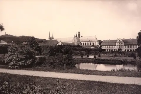 Widok na pałac opatów w Gdańsku z ogrodem i stawem. W oddali wzgórze z pomnikiem.