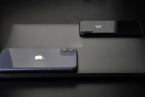 Dwa iPhone'y, w tym jeden fioletowy, leżą na czarnym laptopie. Zastanawiasz się, jak wyłączyć iPhone'a 11?