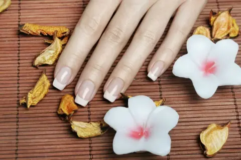 Dłoń z idealnym francuskim manicure, który podkreśla najładniejszy kształt paznokci. Otoczona suszonymi liśćmi i białymi kwiatami.