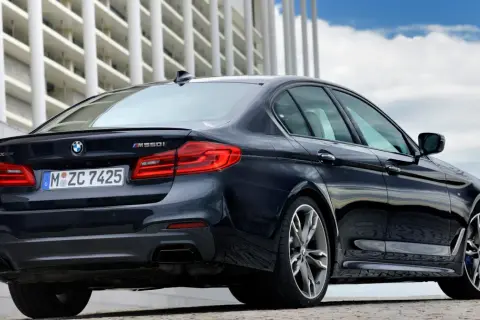 Ciemny BMW m550i z napędem xDrive, z widocznym logo BMW i oznaczeniem modelu, zaparkowany przed nowoczesnym budynkiem.