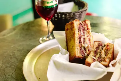 Un delicioso patty melt con carne jugosa y cebolla caramelizada, servido en pan tostado, junto a una copa de vino tinto.
