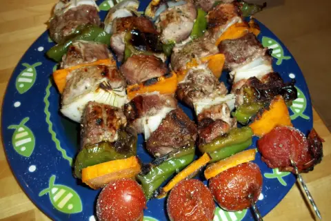 Brochetas de solomillo con pimientos verdes, cebolla y tomate, servidas en un plato azul con dibujos de peces.