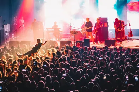Energiczny koncert w klubie Stodoła Warszawa. Tłum szaleje, a na scenie gra zespół. Jedna z fanek jest niesiona przez publiczność.