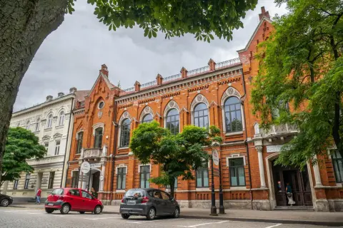 Kamienice w Radomiu, w tym Bank Polski, to ciekawe atrakcje miasta. Dwa samochody zaparkowane na brukowanej ulicy.