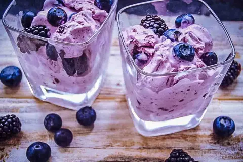 Zwei Gläser mit cremigem, lila gefärbtem frozen joghurt, garniert mit frischen Blaubeeren und Brombeeren.