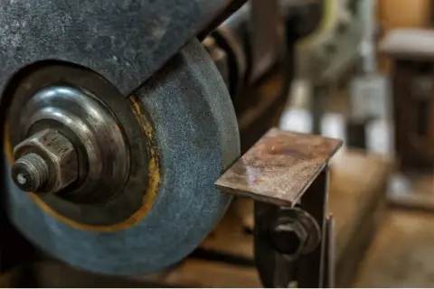 Zbliżenie na kamień szlifierski i metalowy element, pokazujące różne rodzaje kamieni szlifierskich w akcji.