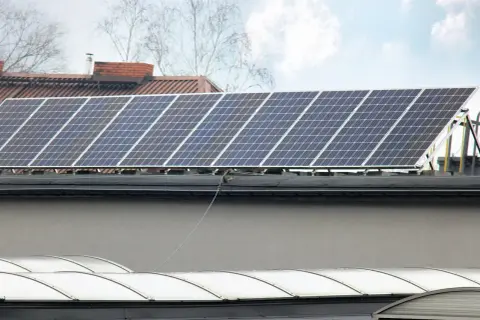 Panele fotowoltaiczne na dachu, gotowe do podgrzewania i produkcji energii. W tle budynki i drzewa.