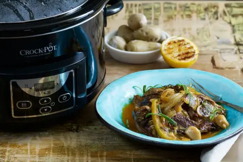 En läcker slow cooker recept med mört kött, citron och rosmarin på en blå tallrik bredvid en Crock-Pot.