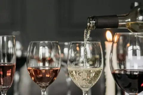Degustacja wina w blasku świec. Nalewanie białego wina do kieliszka, obok różowe i czerwone wino.