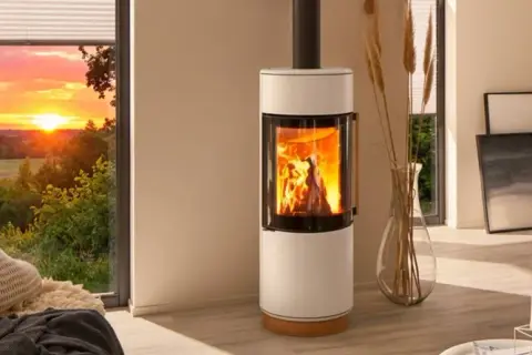 Gemütliches Wohnzimmer mit brennendem Kamin, der die Frage aufwirft: darf man im Sommer den Kamin anmachen? Sonnenuntergang draußen.
