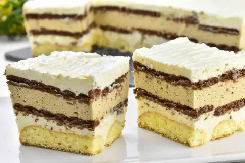 Pyszne ciasto caffe latte z warstwami biszkoptu, kremu kawowego i czekolady, zwieńczone bitą śmietaną.
