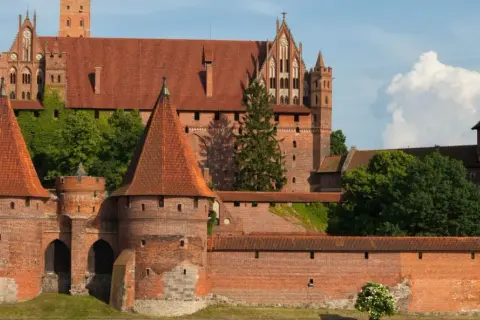 Potężny zamek w Malborku, wpisany na listę UNESCO w Polsce, z czerwonymi dachami i zielenią.