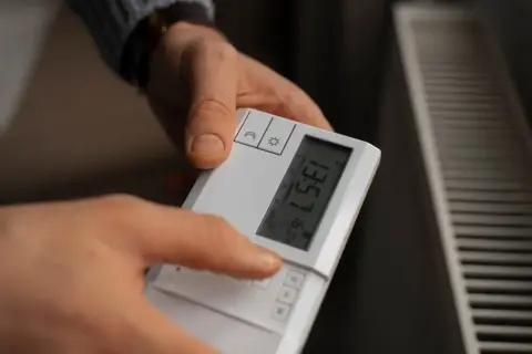 Ręce ustawiają sterownik pieca gazowego. Na ekranie widoczna jest temperatura 16.0°C.