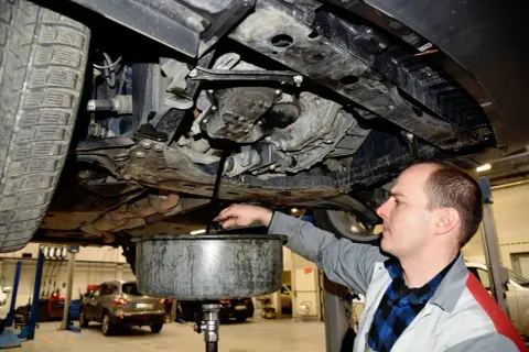 Mechanik wymienia olej w samochodzie, zbierając zużyty płyn do miski.