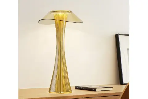 Elegancka, złota lampka stołowa o smukłej, prążkowanej podstawie i szerokim kloszu, tworząca ciepłe światło.