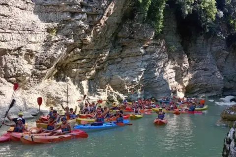 Gruppo in canoa esplora un canyon con pareti rocciose imponenti, navigando tra le marmitte dei giganti scavate dall'acqua.