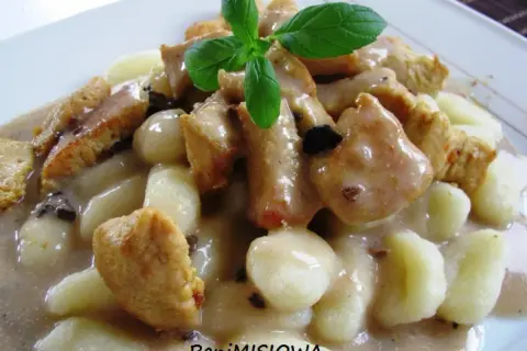 Pyszne gnocchi z kurczakiem w sosie śmietanowym, udekorowane listkiem bazylii. Danie wygląda apetycznie i sycąco.
