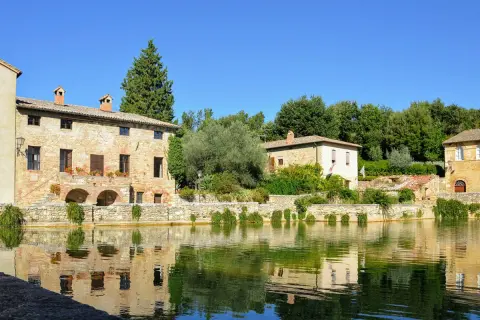 Antica sorgente termale con edifici in pietra e riflessi sull'acqua, un incantevole scorcio dei borghi del Val d'Orcia.