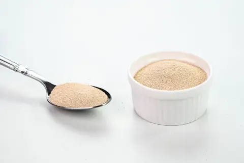 Levure sèche dans une cuillère et un ramequin blanc. Comprendre la différence entre levure chimique et bicarbonate de soude est essentiel pour la pâtisserie.