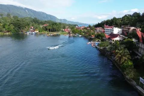 Ein Boot rast über den See, während man die Hügel und Häuser von Sumatra beim Backpacking genießt.