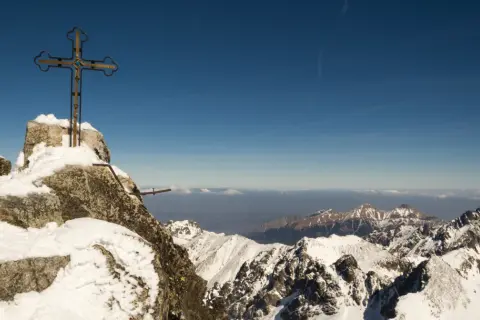 Szczyt Gerlach bez przewodnika. Krzyż na skalistym, ośnieżonym wierzchołku, w tle zimowe Tatry i błękitne niebo.