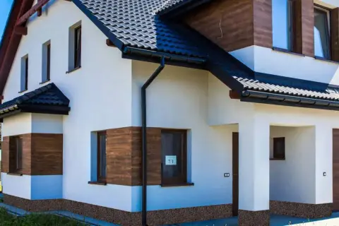 Nowoczesny dom z białym tynkiem, drewnianymi akcentami i kamiennym cokołem na elewacji.