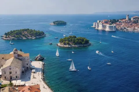 Un día perfecto para tu ruta Croacia 7 días: veleros navegan en aguas turquesas cerca de islas verdes y la histórica ciudad amurallada.