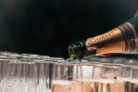 Versando champagne da una bottiglia in una fila di bicchieri, mostrando diversi tipi di champagne.