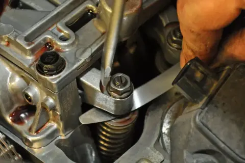 Mechanik reguluje zawory w silniku, używając śrubokręta i cienkiego metalowego narzędzia.