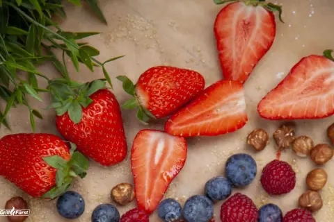 Frische Erdbeeren, Blaubeeren und Himbeeren liegen bereit, um sie einzufrieren. Ein paar Haselnüsse und grünes Blattwerk runden das Bild ab.